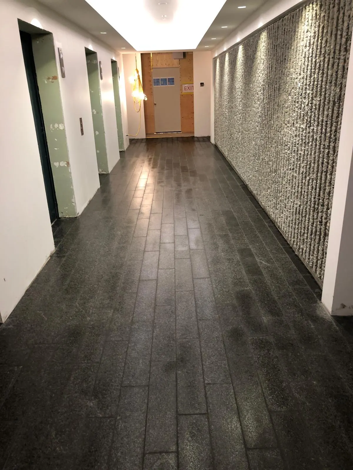 Finished elevator lobby corridor with dark stone-look tile flooring and a textured feature wall, from the Eckler 980 common area renovation