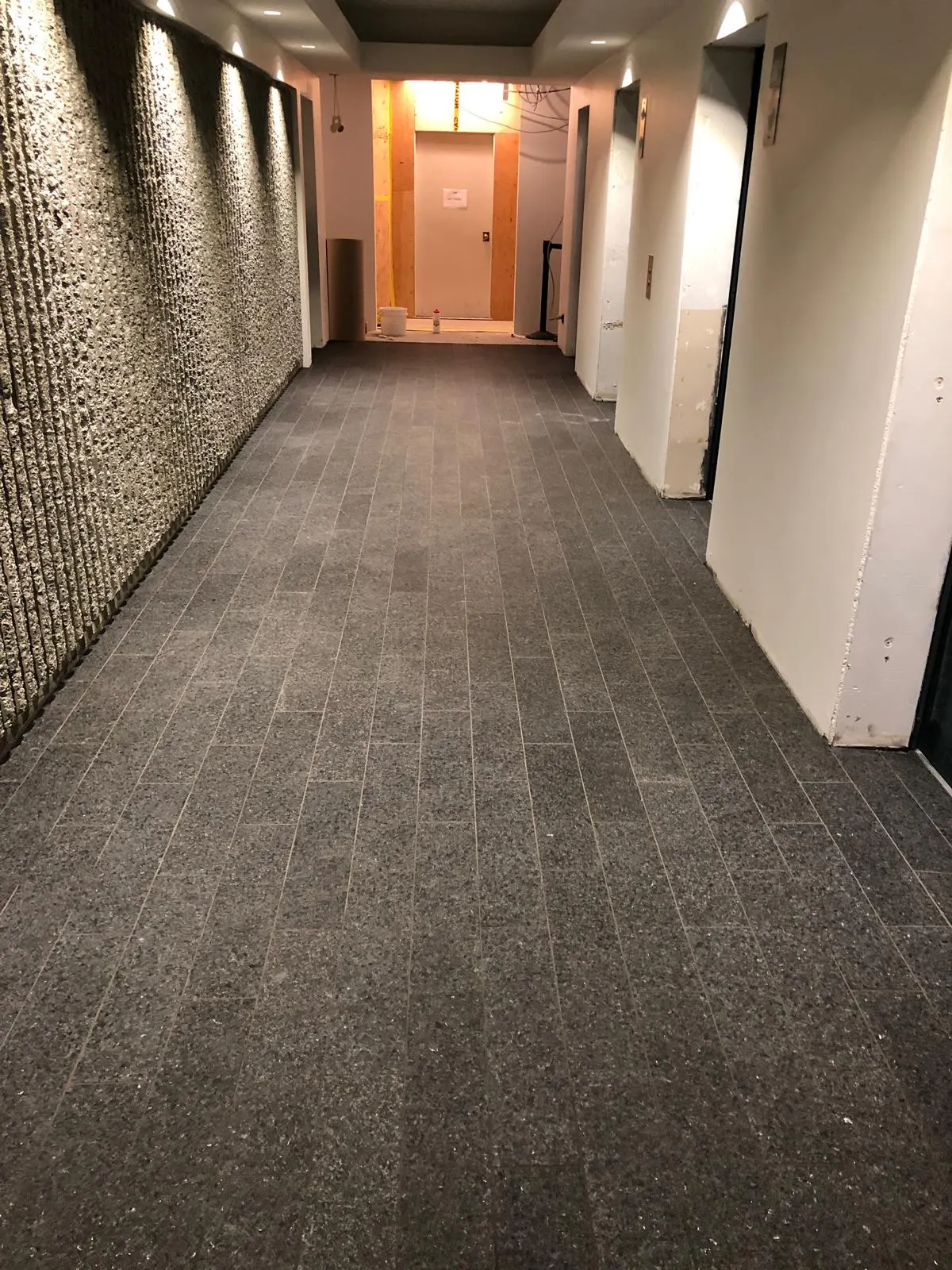 Finished elevator corridor with dark tile flooring and a textured stone feature wall, framing in progress at the far end