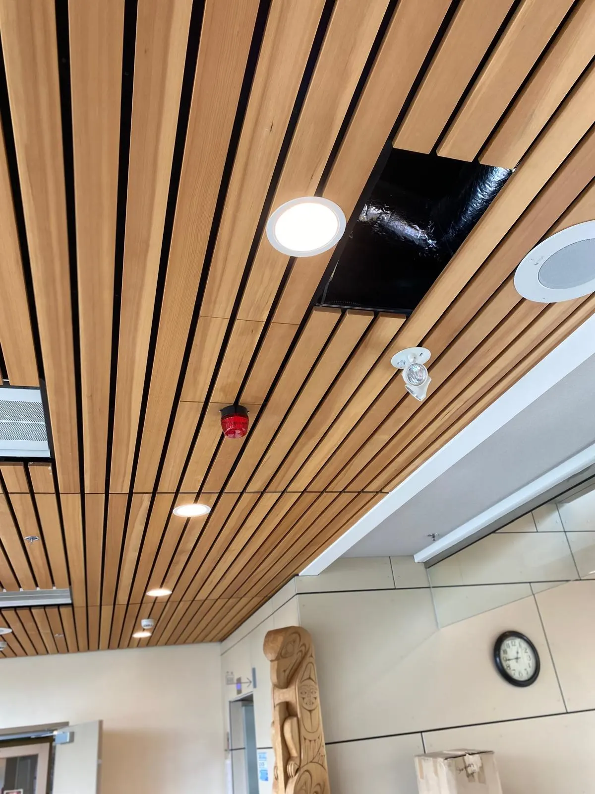 Finished lobby with a wood slat ceiling, recessed lighting, and Indigenous carved artwork against a tiled feature wall