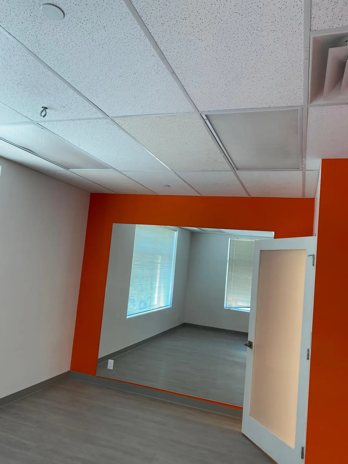 The same office suite seen from the corridor, orange accent wall framing the open entry door