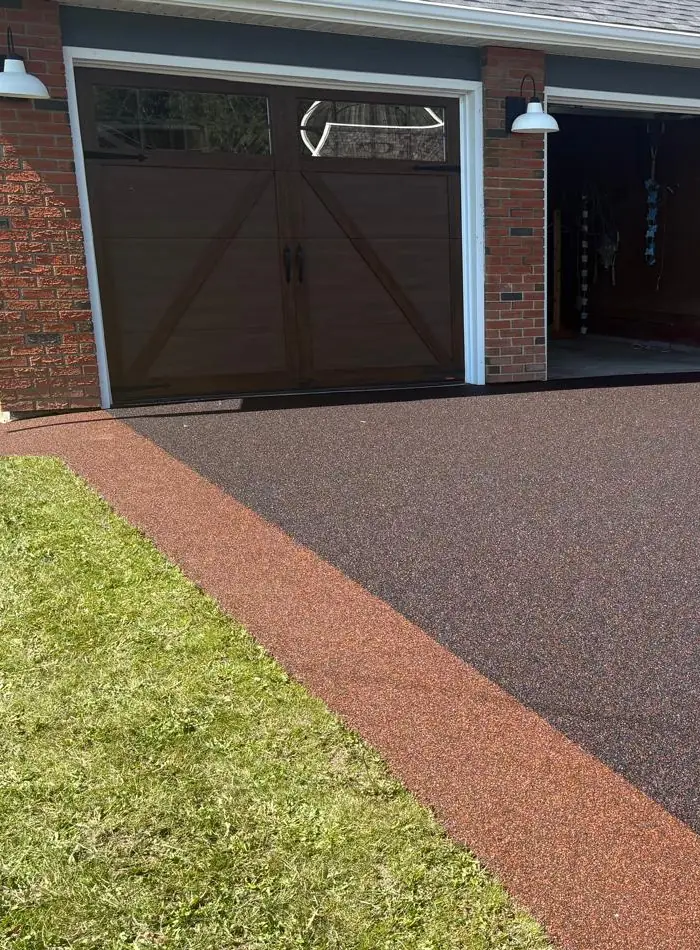 After: the same acreage driveway surfaced in dark terracotta poured rubber with a lighter red inlaid border