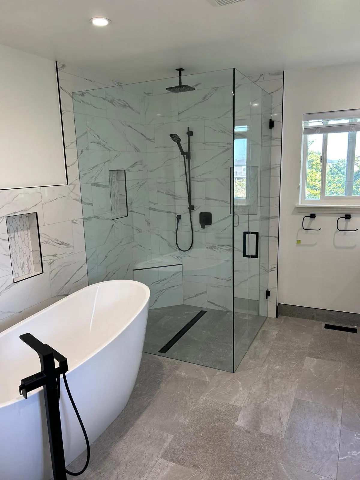 Finished bathroom with a freestanding soaker tub and a glass-enclosed marble tile shower with black fixtures
