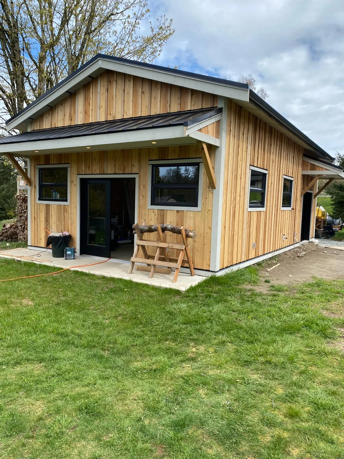 Finished cedar-sided cabin with a black standing-seam metal roof, covered entry, and large windows on a rural property
