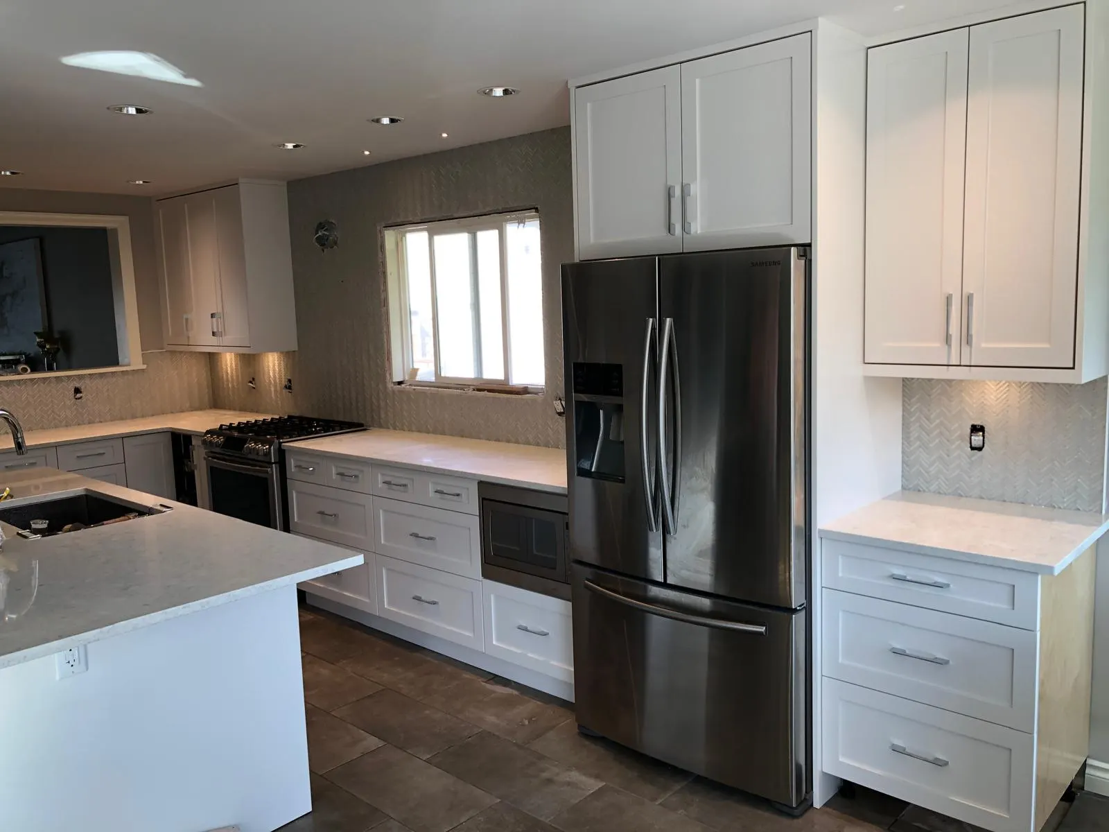 Finished kitchen with white shaker cabinets, herringbone tile backsplash, quartz countertops, and stainless steel appliances