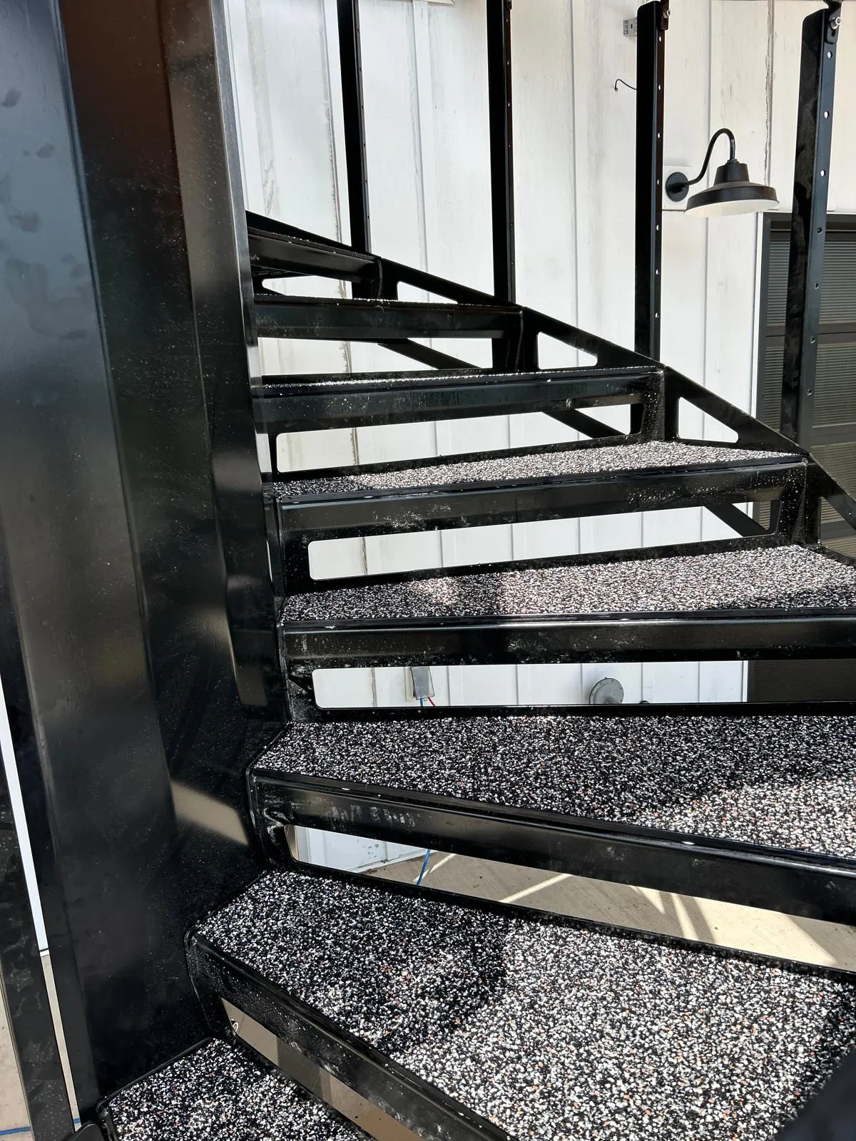 Finished exterior metal staircase with treads and landings resurfaced in black, white, and orange-flecked poured rubber